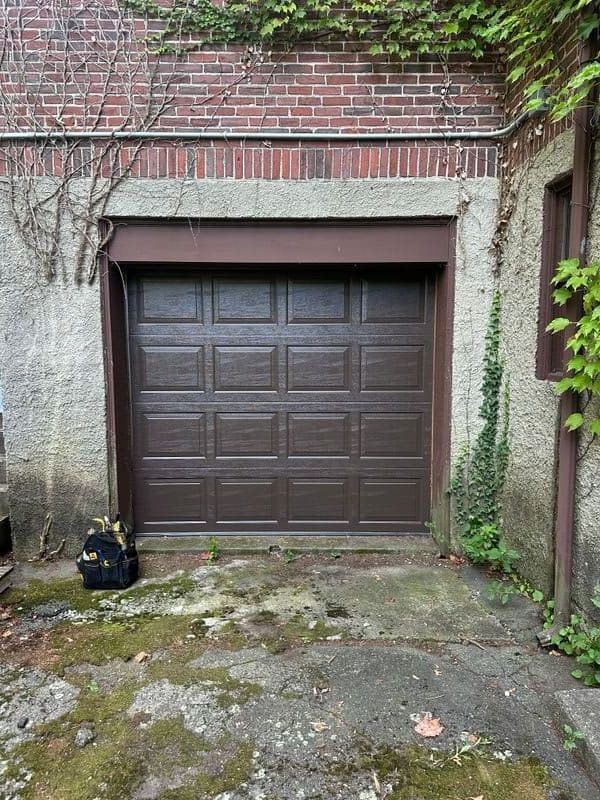 Dark brown raised-panel garage door on brick home with ivy