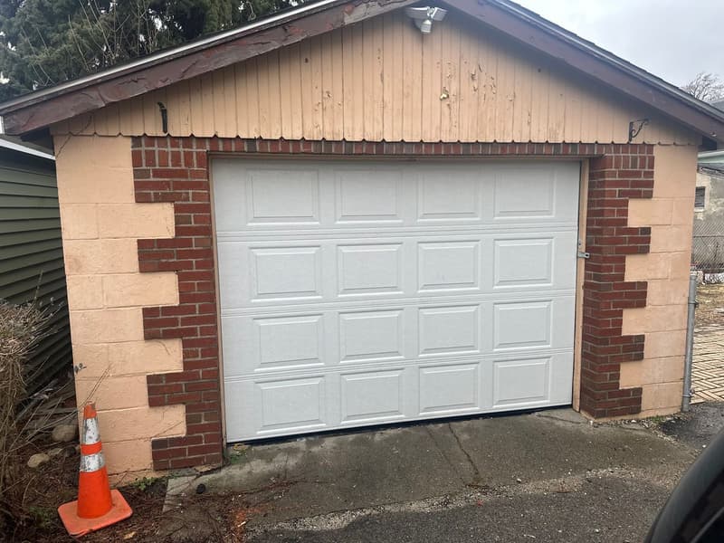 White raised-panel garage door installed on brick and block detached garage